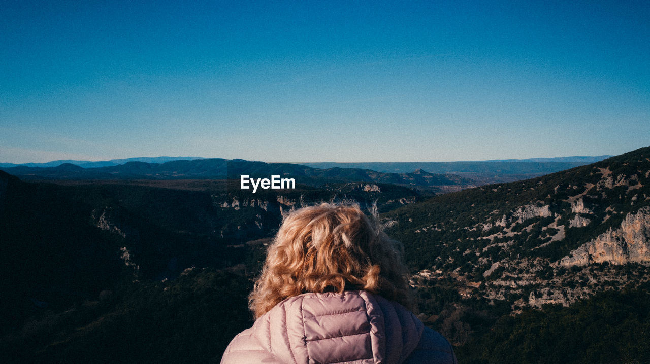 Rear view of woman standing on mountain against blue sky