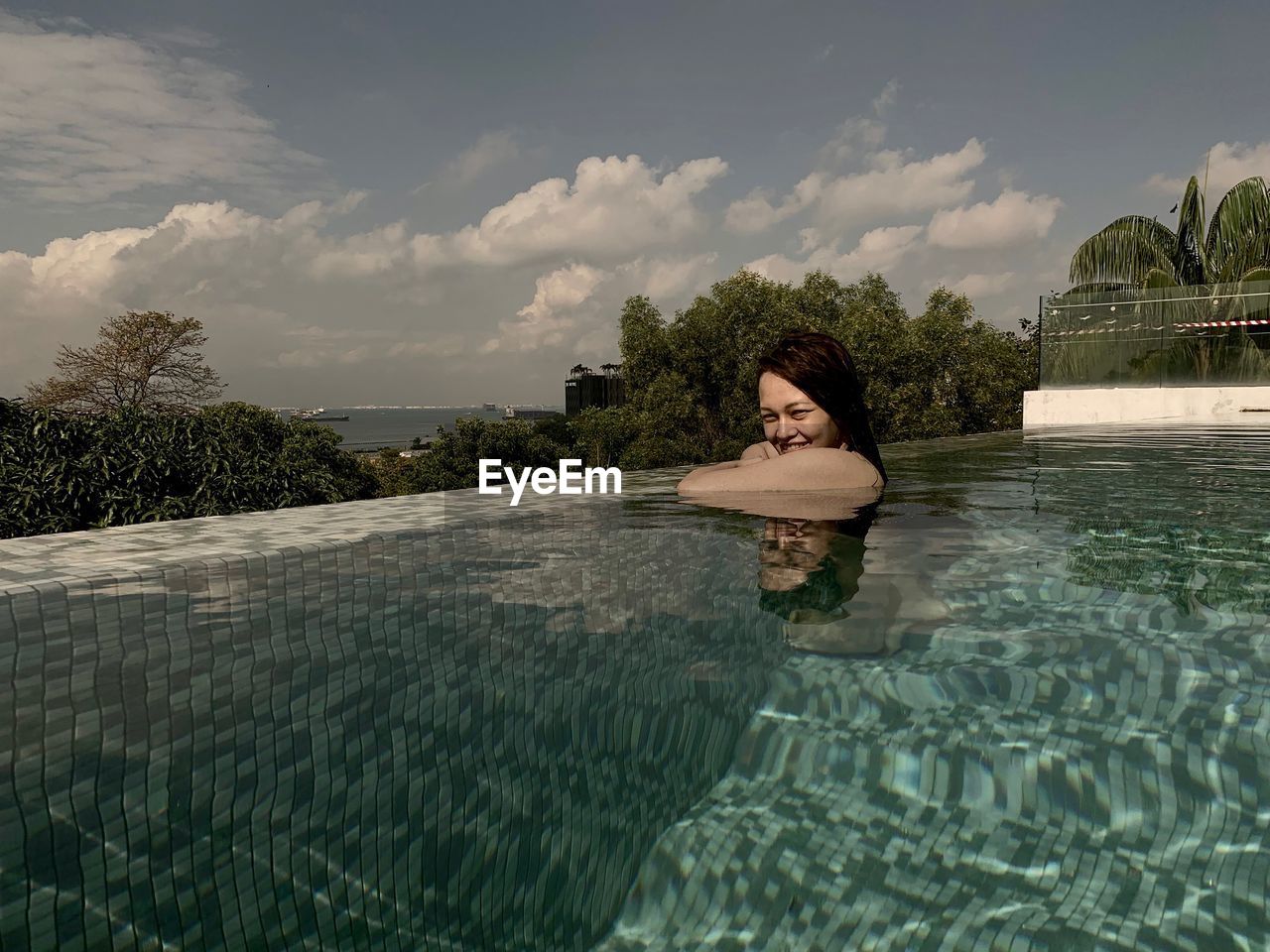 Portrait of smiling woman in swimming pool against sky