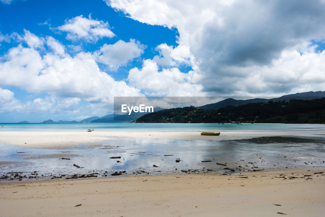 Boat anchored on sand by sea with mountains against cloudy sky