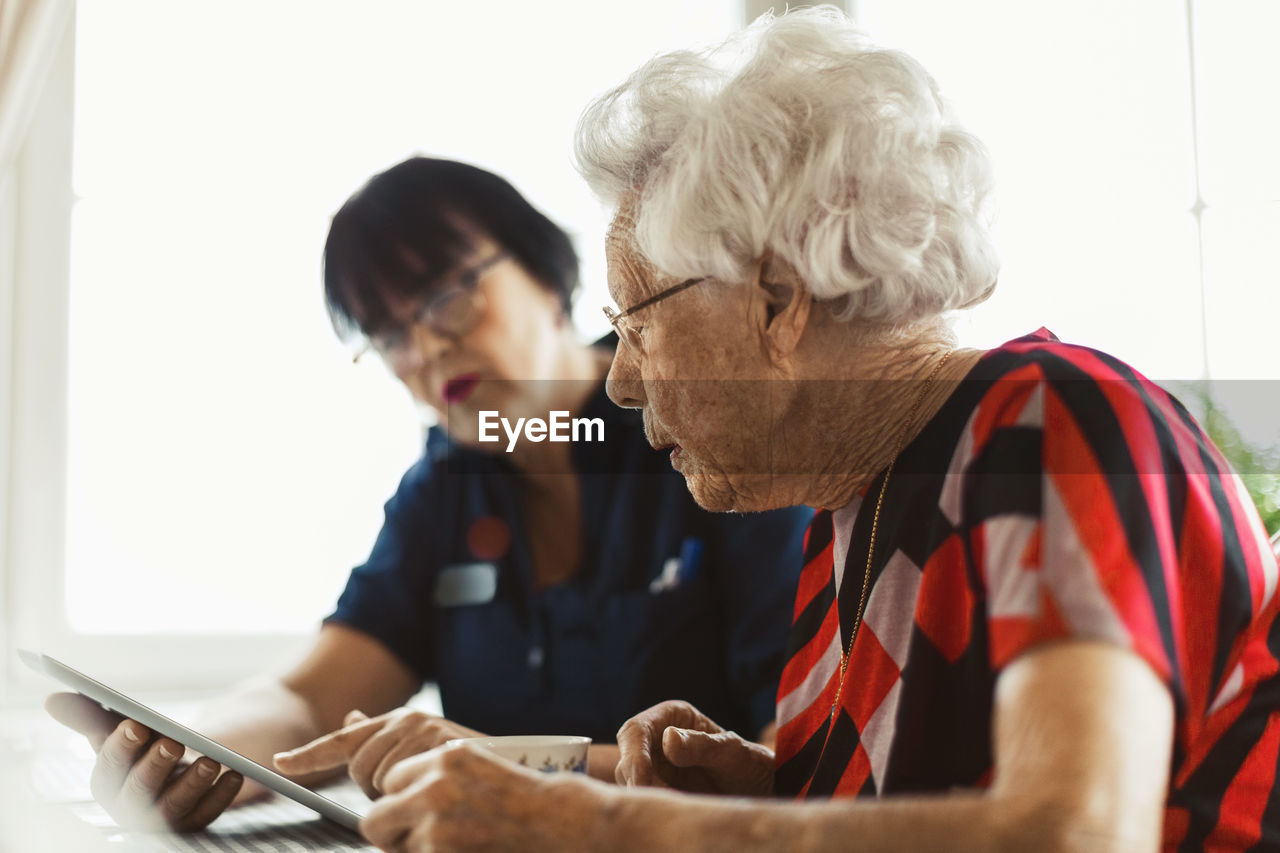 Senior woman using digital tablet with caretaker at home