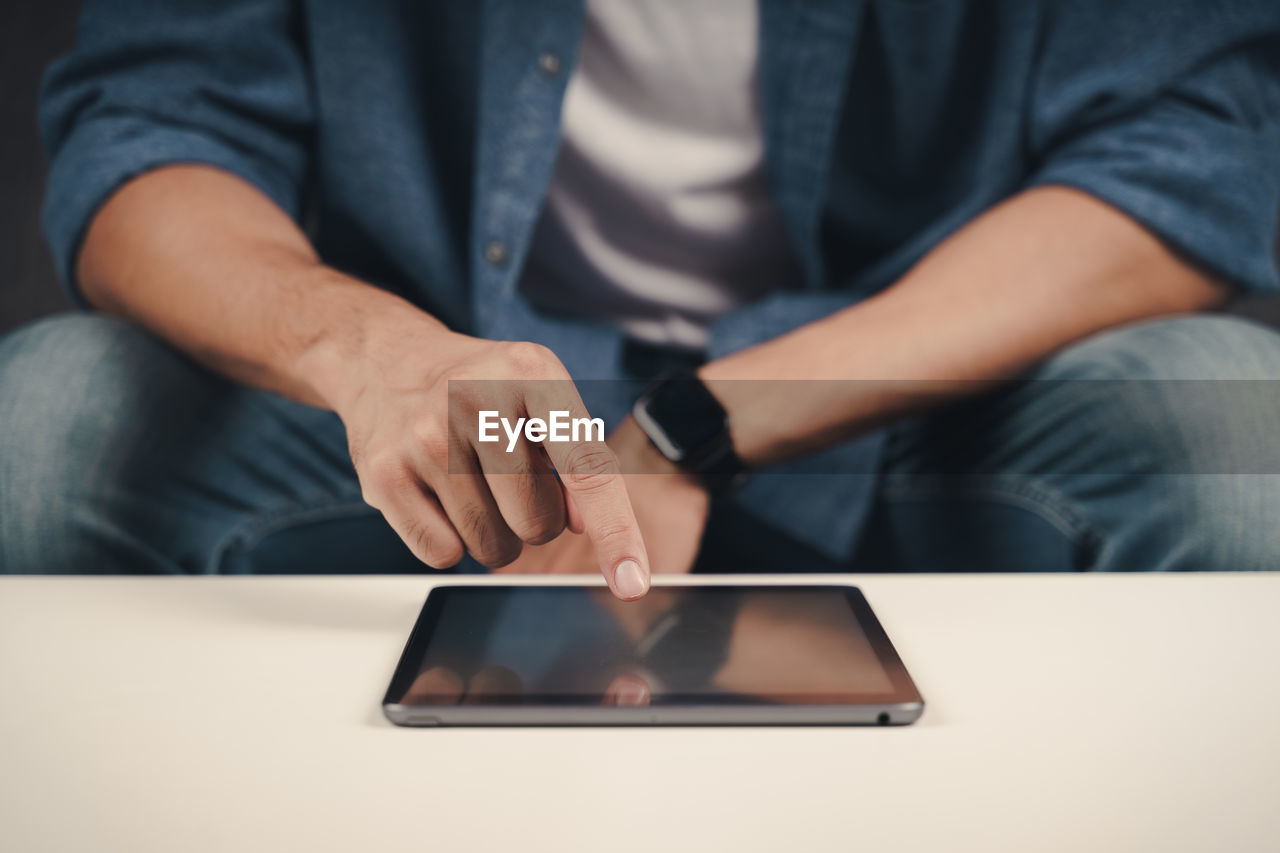 MIDSECTION OF MAN USING LAPTOP ON TABLE