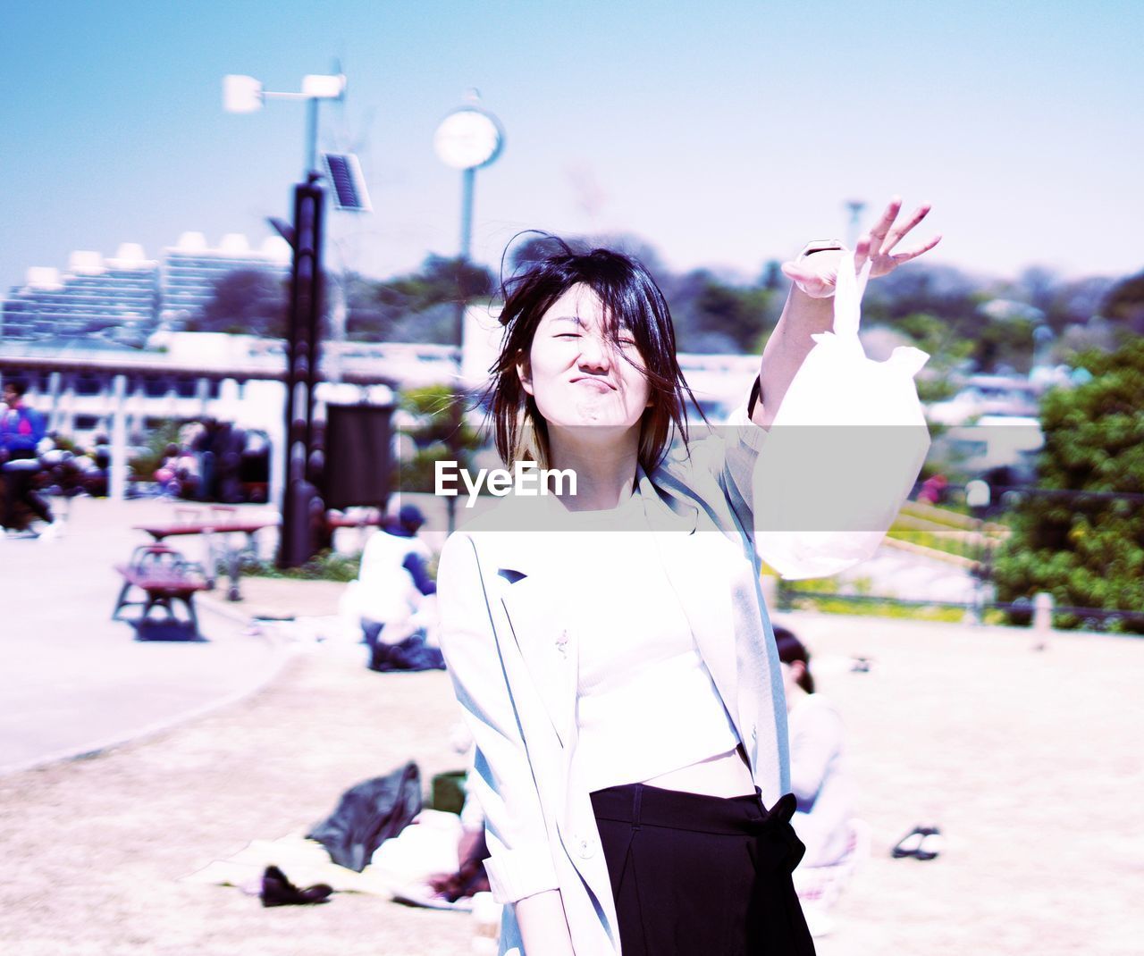 Portrait of smiling young woman holding plastic bag while making a face against sky