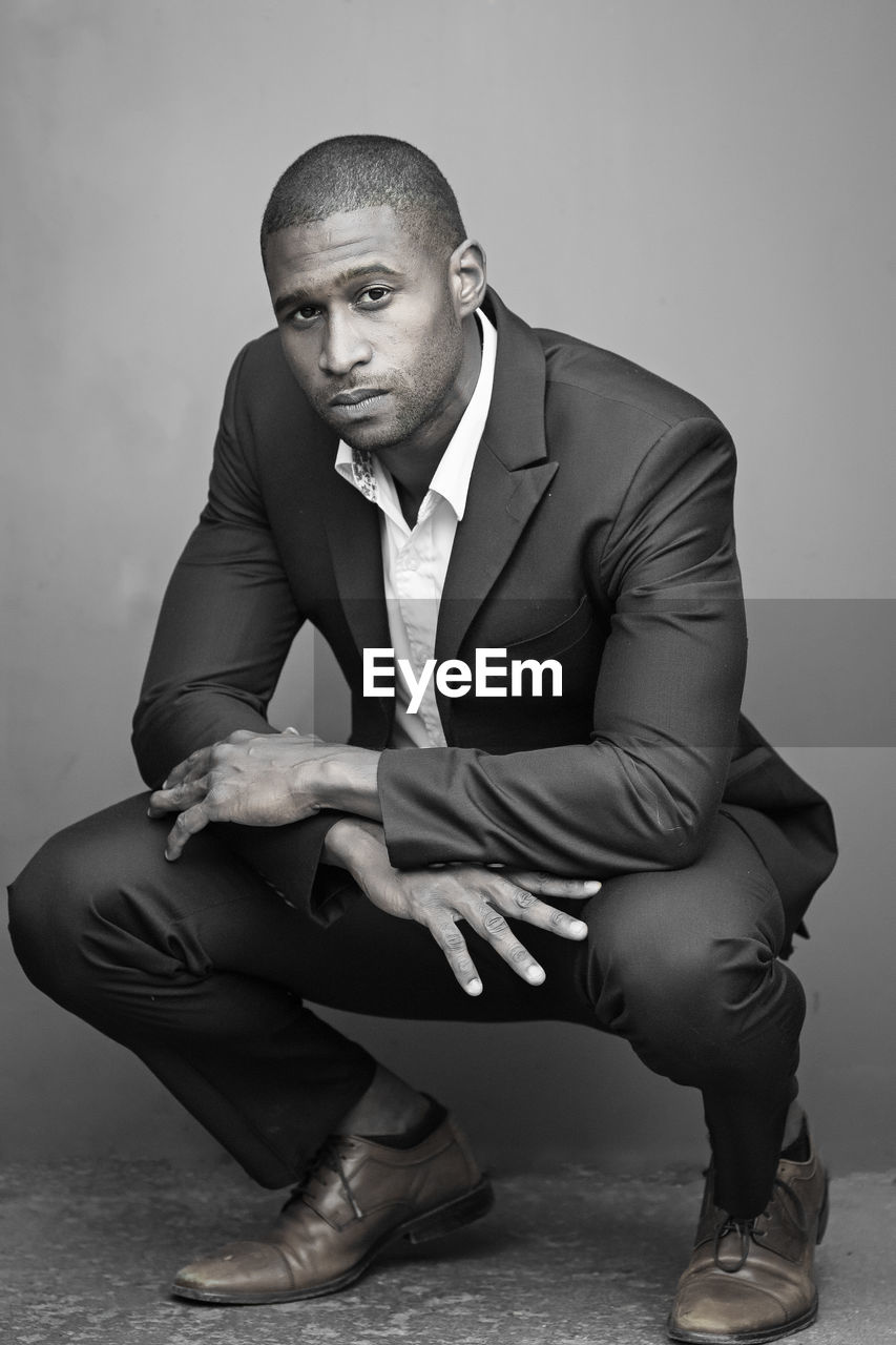 Portrait of businessman wearing blazer crouching against wall