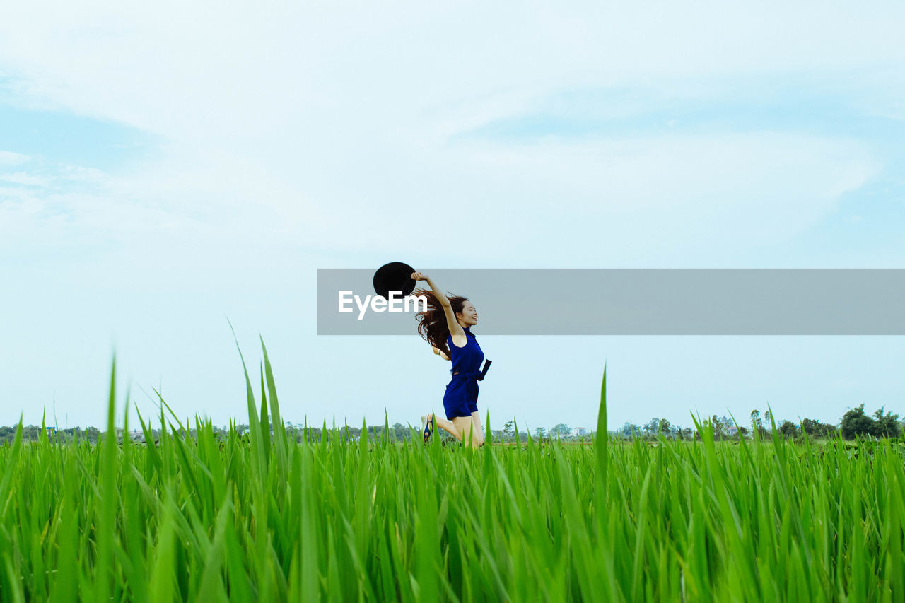 Carefree woman running in rice field against sky