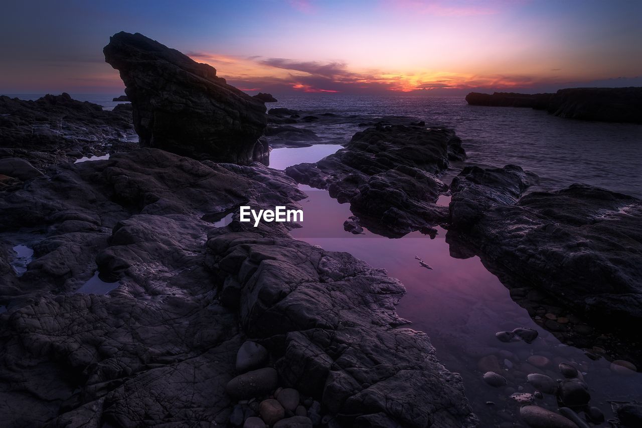 Rock formation at beach against sky during sunset