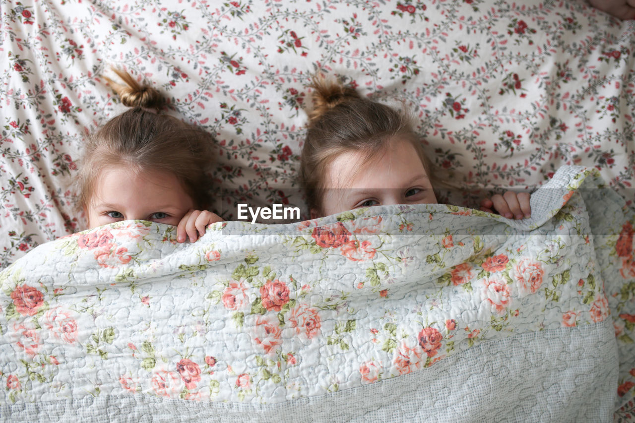 Funny children embrace, play under a blanket on the bed. concept happy childhood and siblings. 