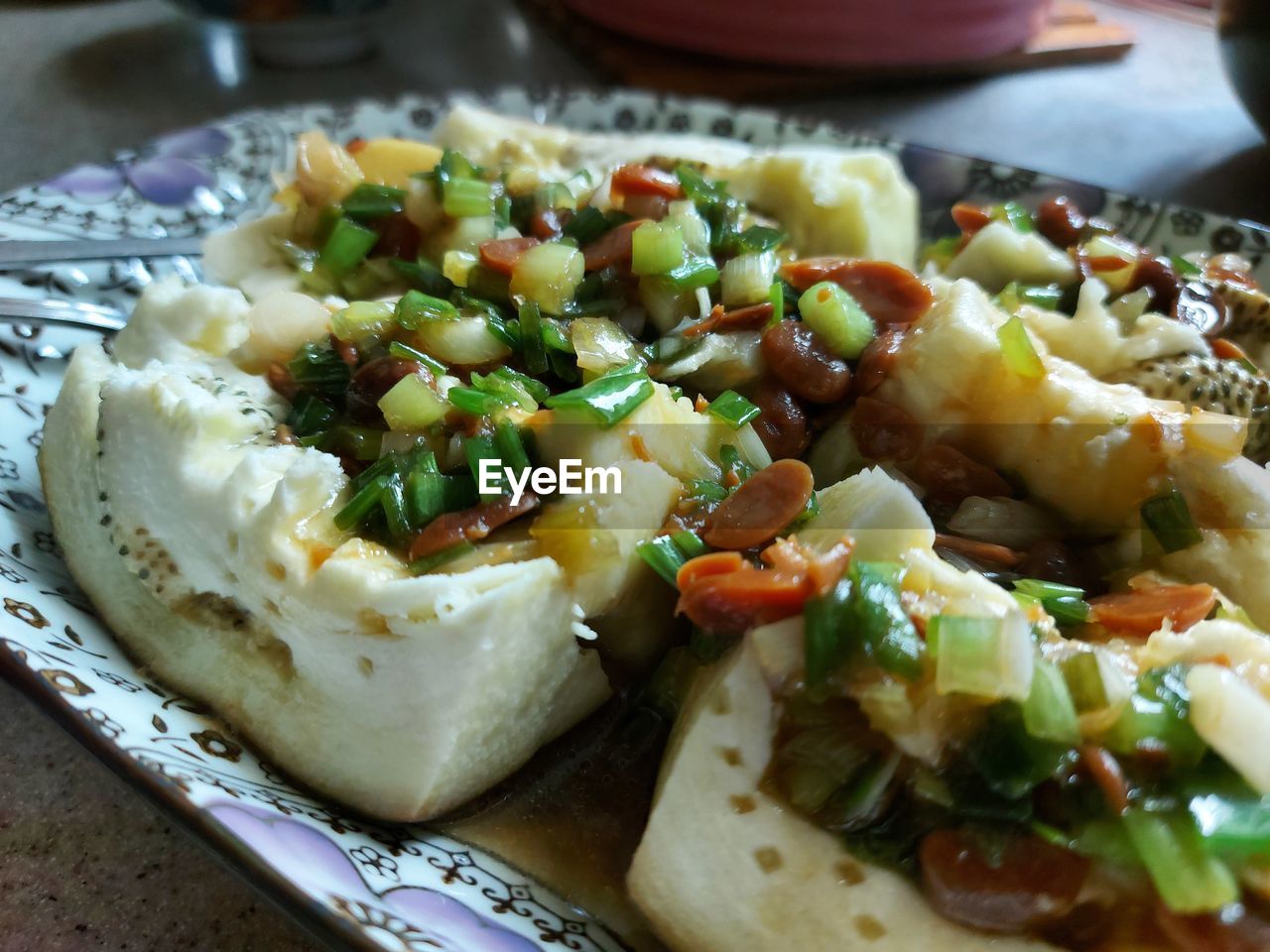 Close-up of steamed eggplant topped with beans and spring onions