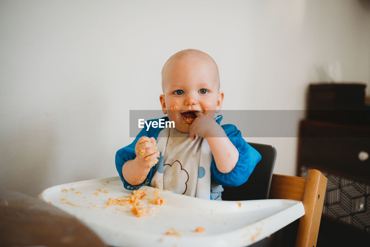 Adorable baby learning how to eat making a mess finger in mouth