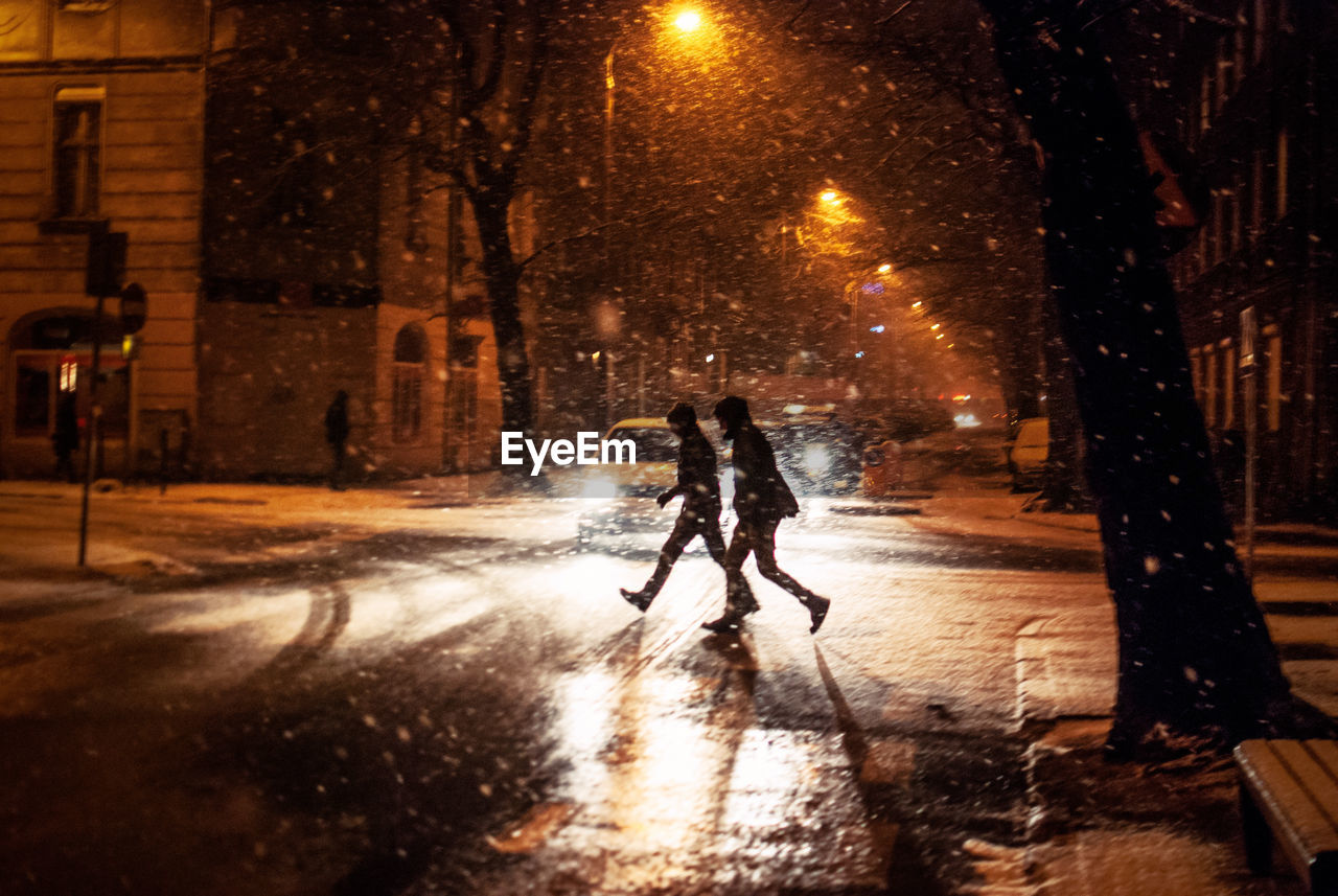 People crossing road during snowfall in city at night