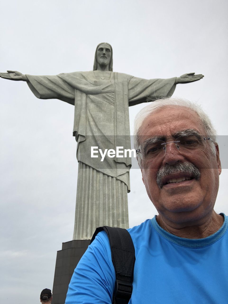 Low angle portrait of man against jesus christ statue and sky