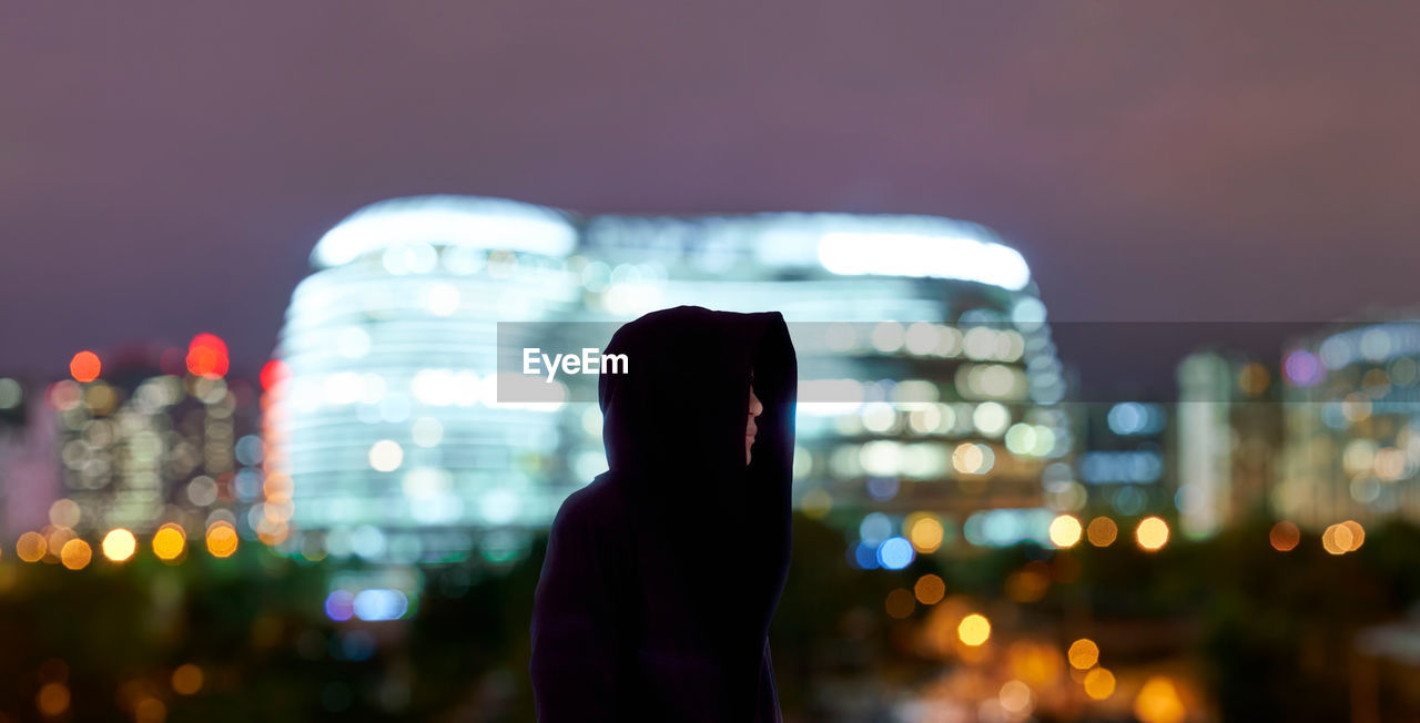 Man standing against illuminated city at night