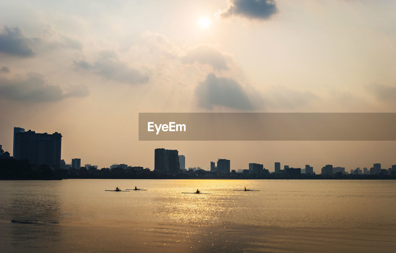 Silhouette buildings by sea against sky during sunset