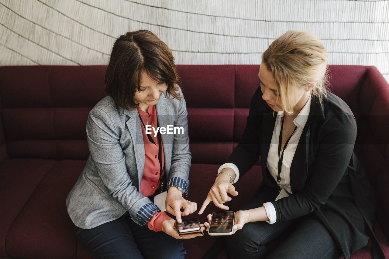 Businesswomen discussing over smart phones while sitting on sofa at convention center