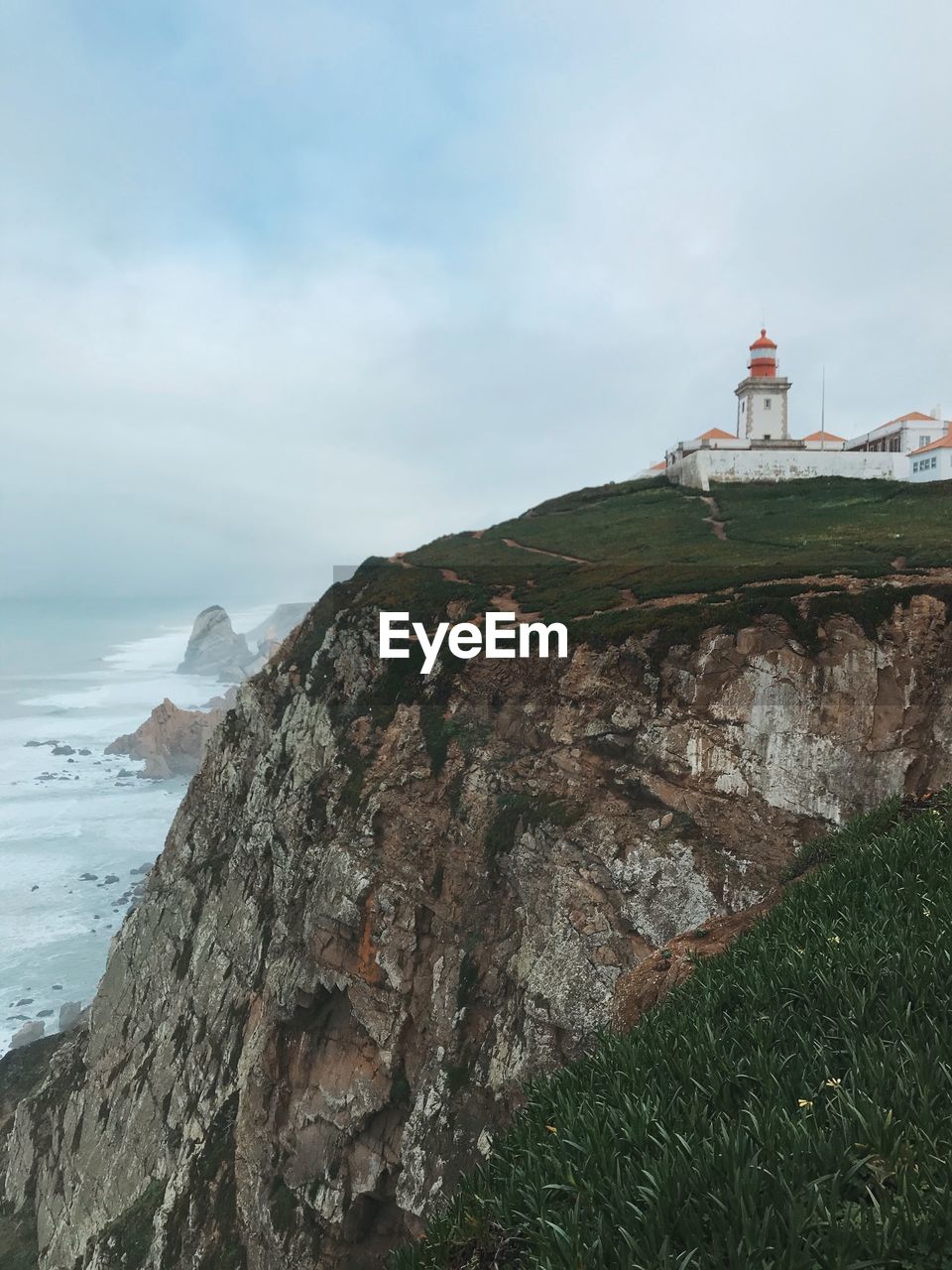 LIGHTHOUSE ON SEA BY MOUNTAIN AGAINST SKY