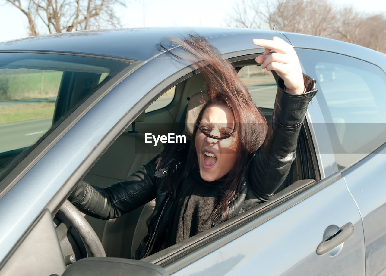 Portrait of young woman in car showing obscene gesture