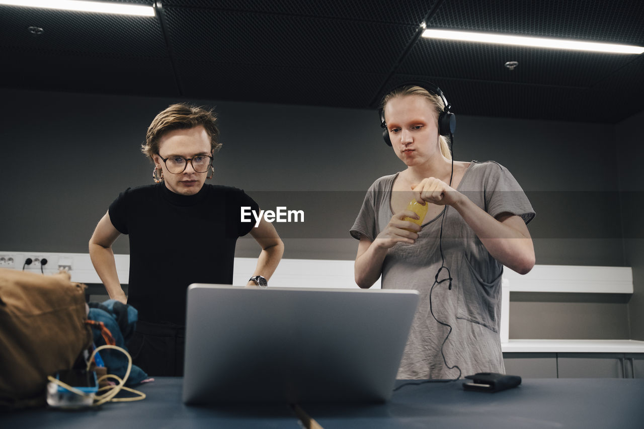 Young androgynous colleagues looking at laptop while standing in office