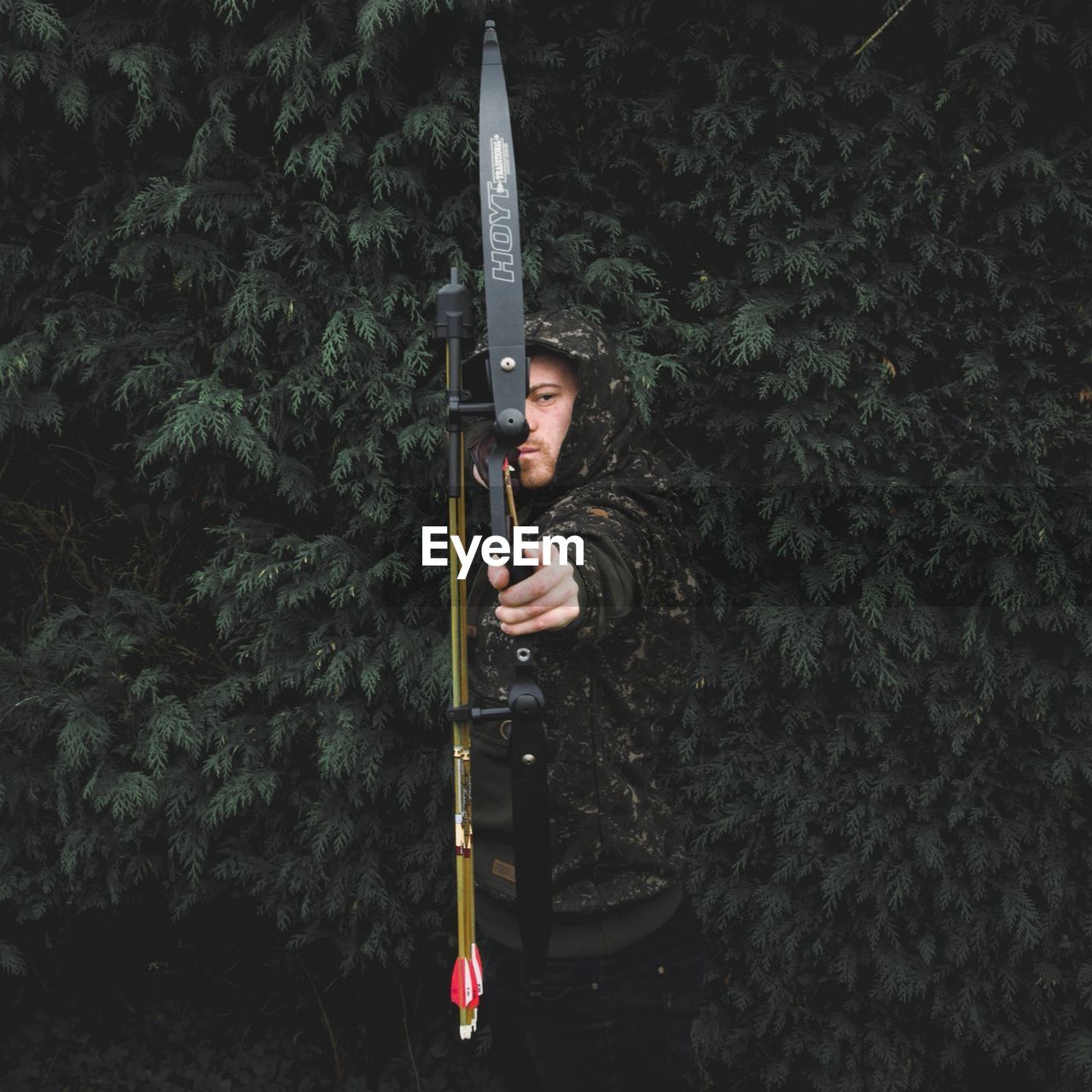 PORTRAIT OF YOUNG MAN WITH UMBRELLA STANDING BY PLANTS