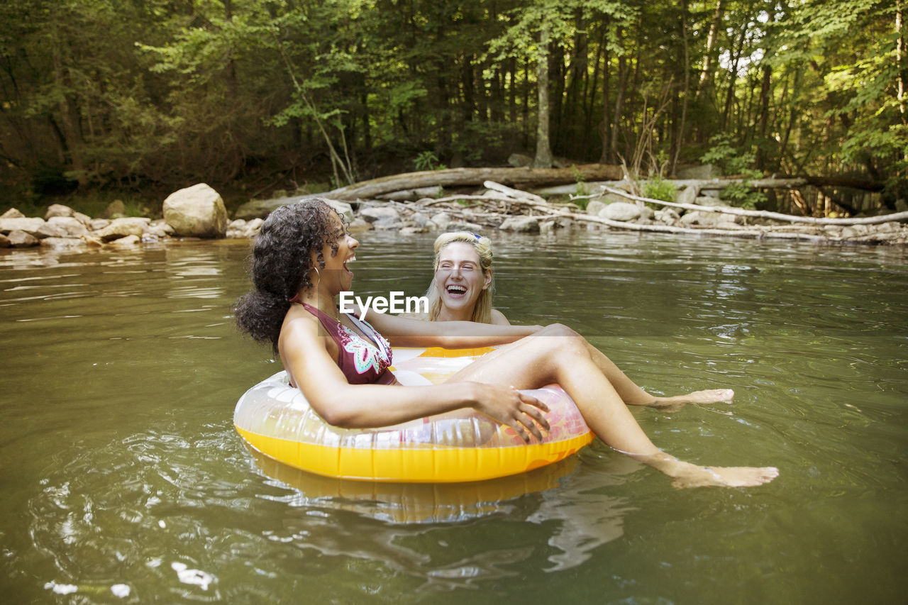 Cheerful female friends laughing using inner tubes in river