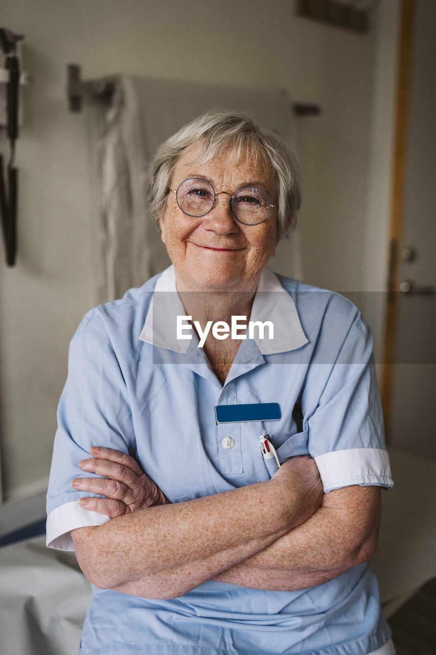 Portrait of smiling senior female doctor standing with arms crossed