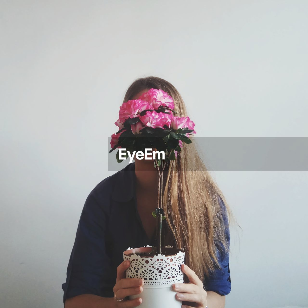 Woman holding flower against wall at home