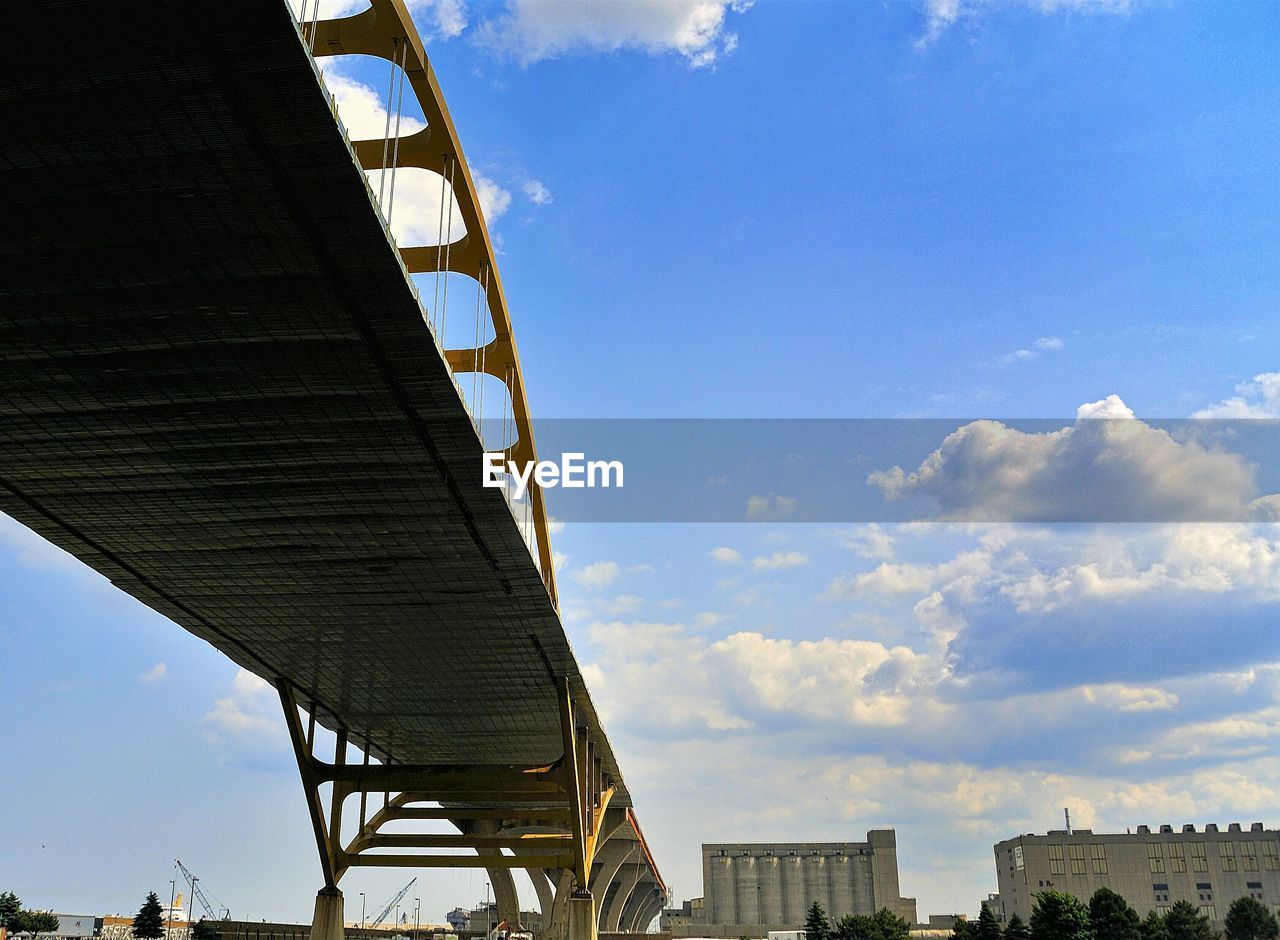 Low angle view of bridge by buildings against sky