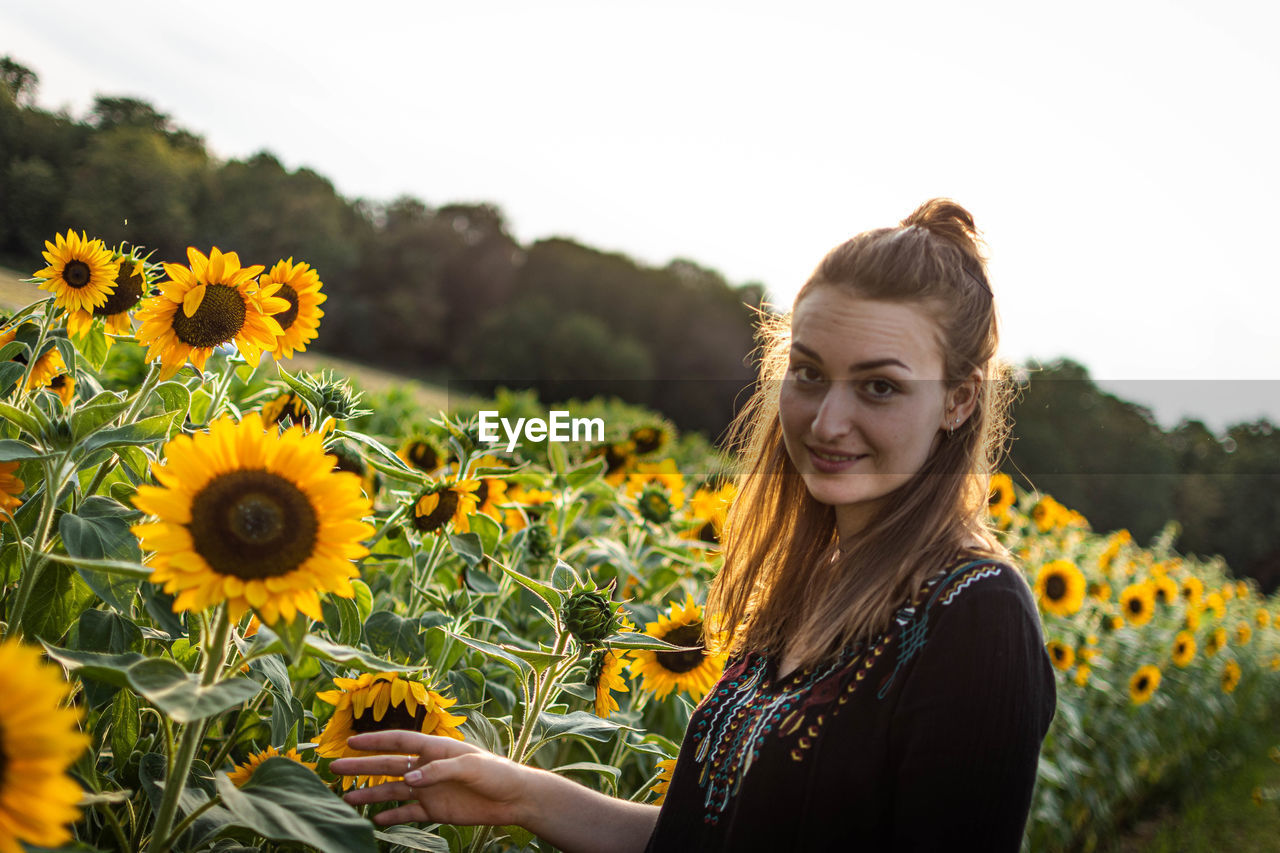 PORTRAIT OF SMILING YOUNG WOMAN AGAINST SUNFLOWER