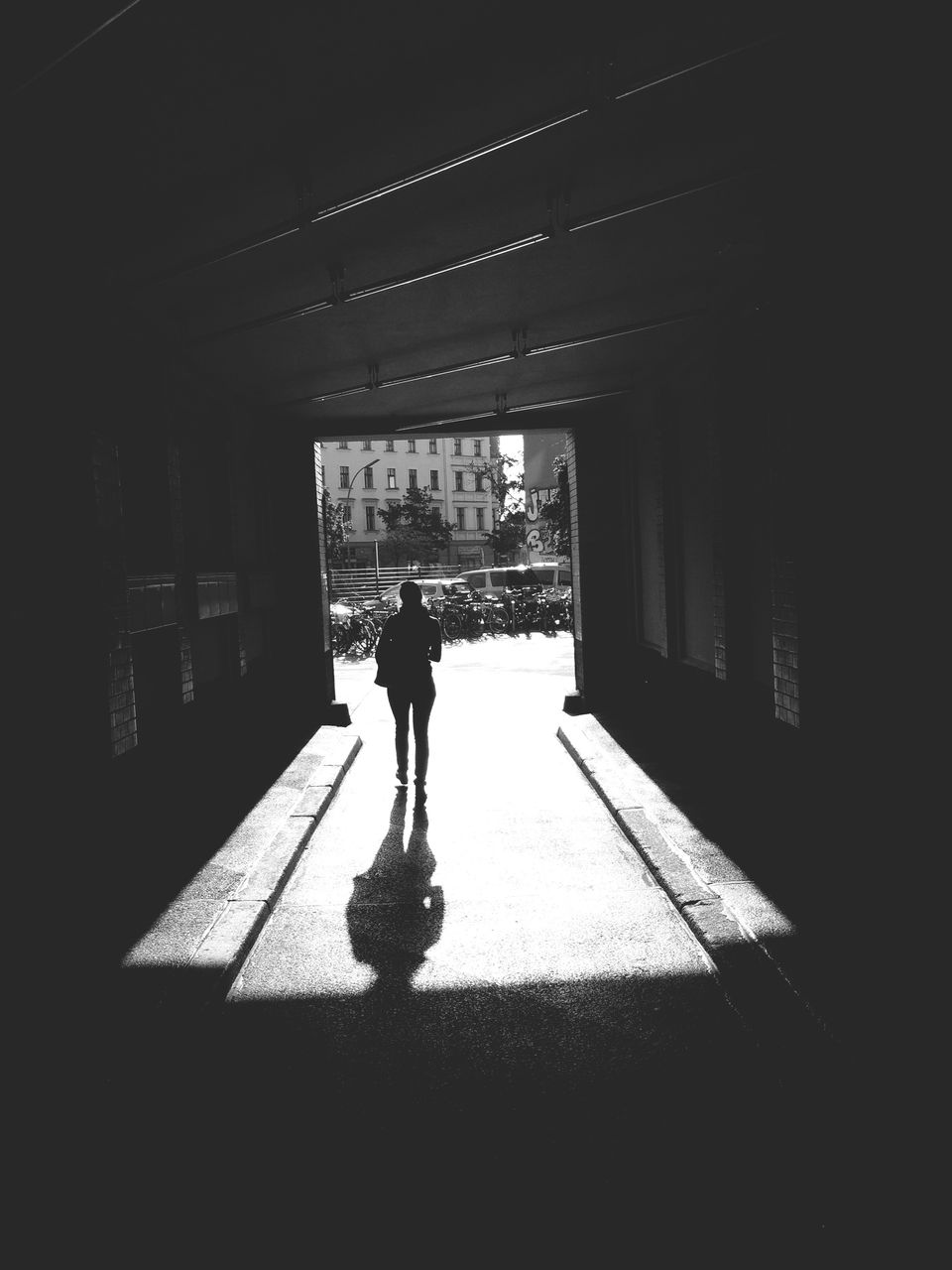 Full length rear view of woman walking through tunnel towards street