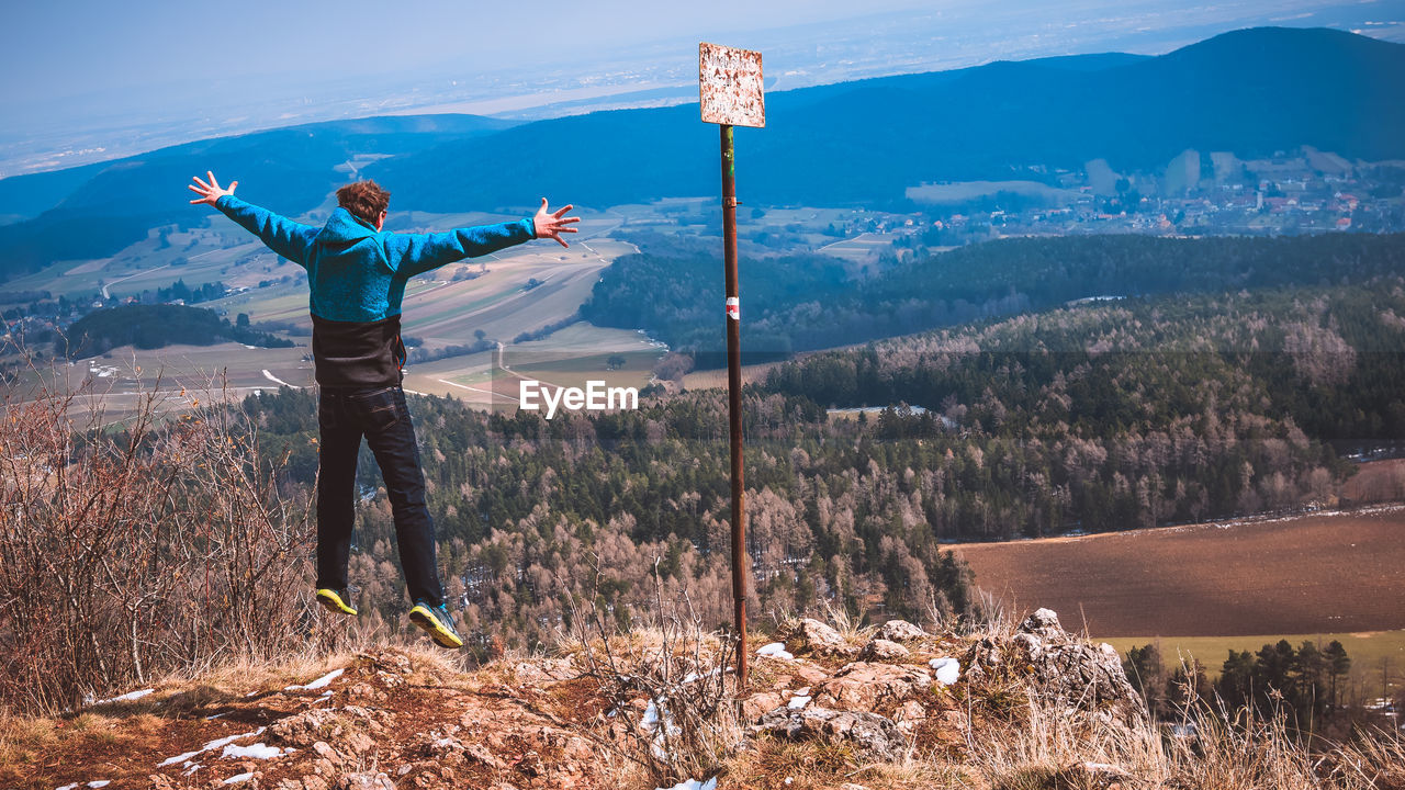 Rear view of man jumping over landscape against mountains