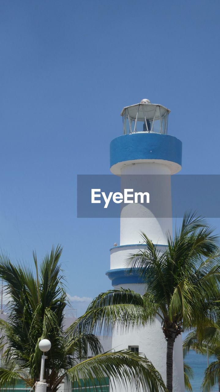 Blue and white colored lighthouse by sea against clear sky