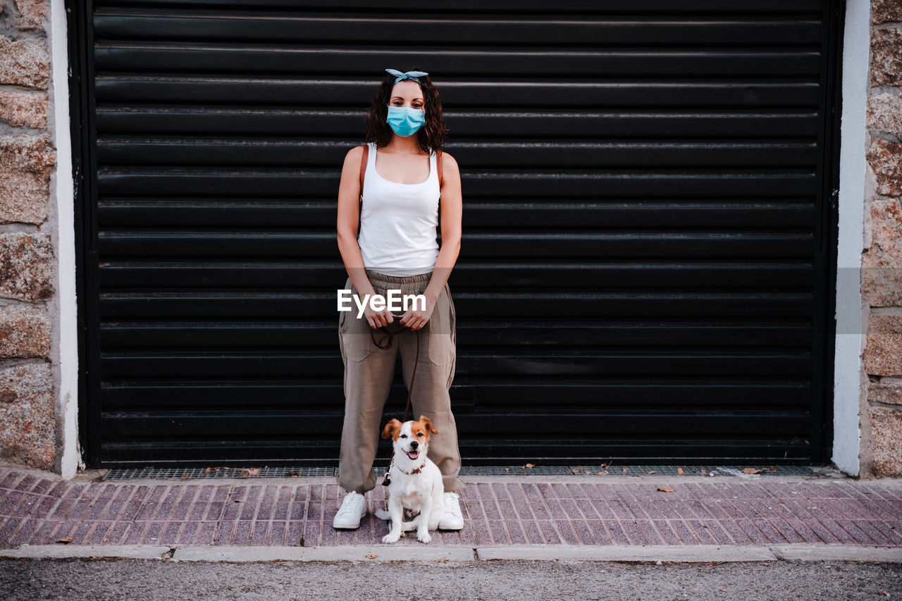 Full length of woman with dog against shutter