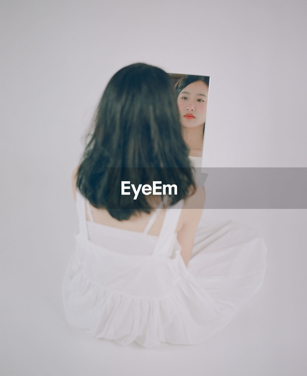 Rear view of woman looking in mirror against white background