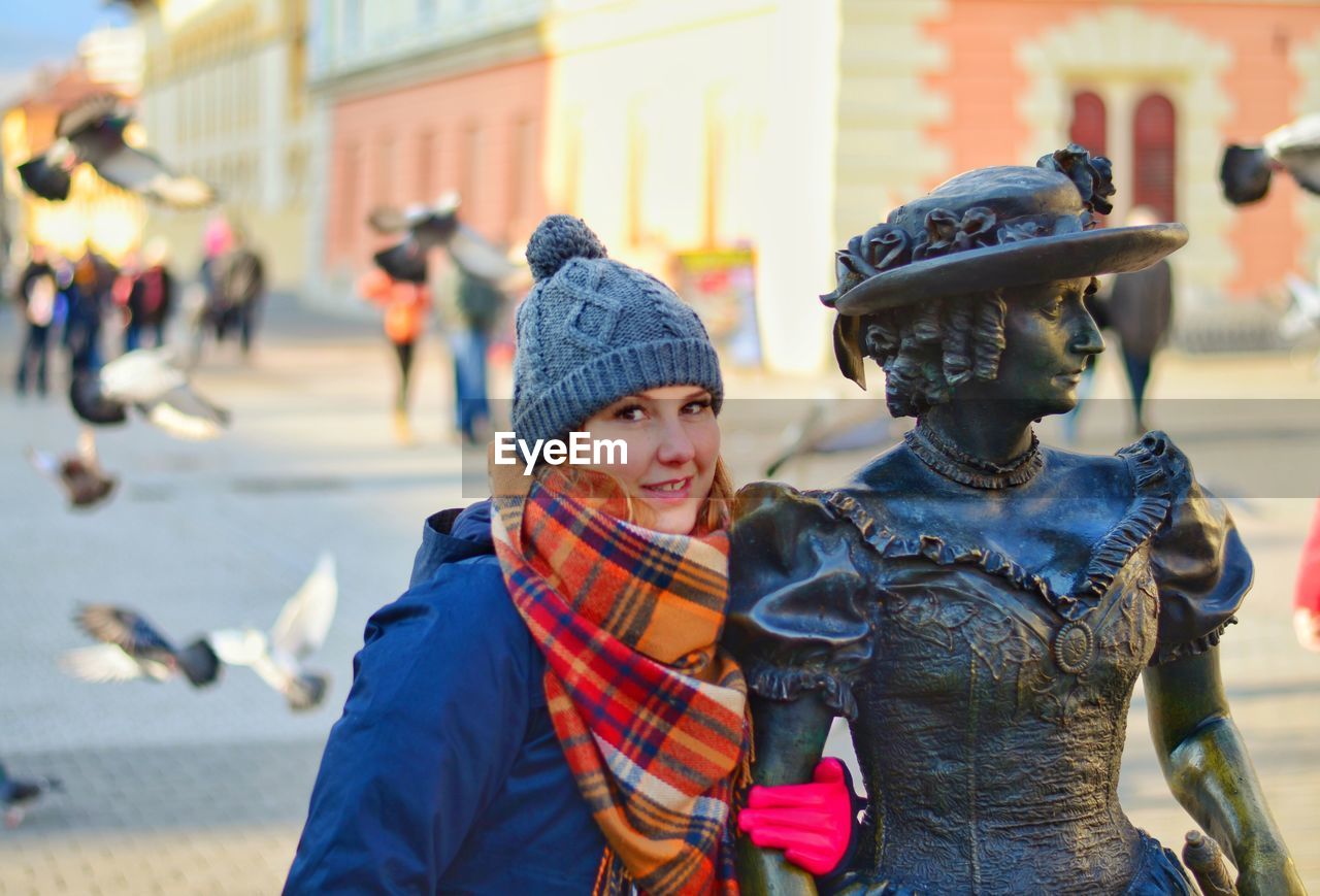 Portrait of woman standing by metallic statue in city