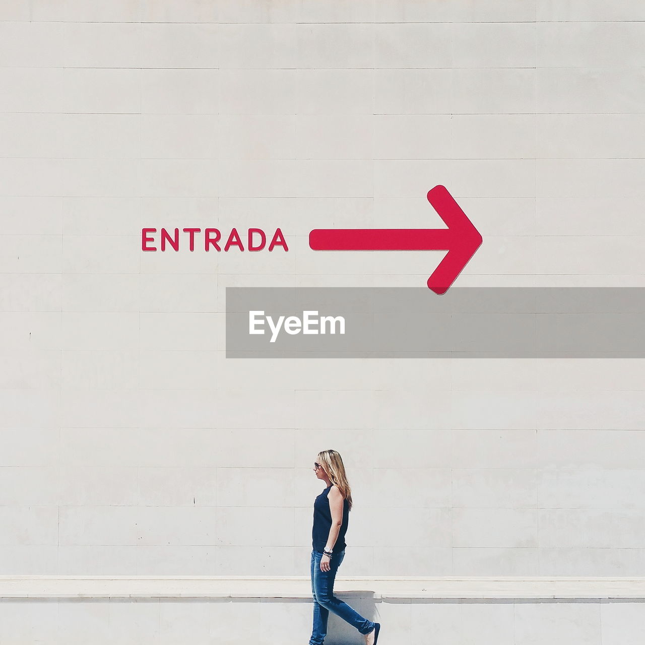 Profile view of woman walking by wall with entrance sign and arrow symbol