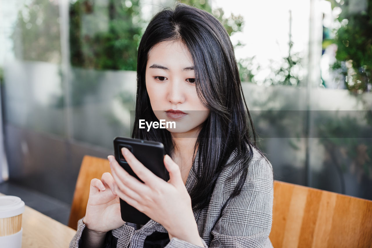 Professional chinese entrepreneur woman working on mobile phone in cafeteria. technology, lifestyle