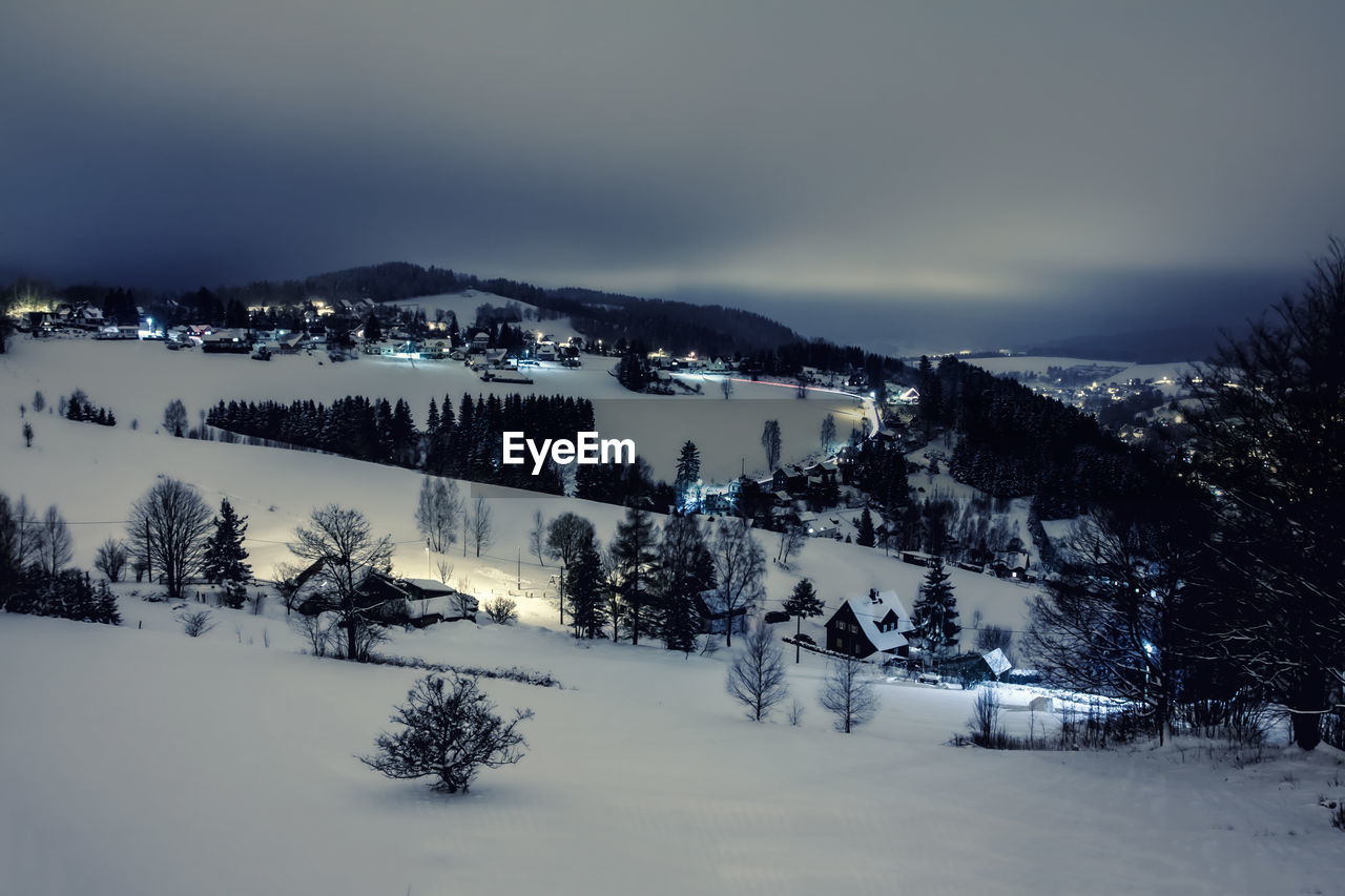 High angle view of houses and trees on snow covered field against sky at dusk