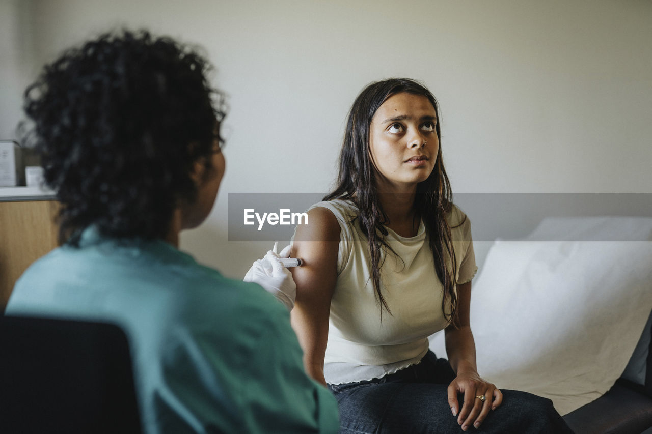 Female doctor giving vaccine to young woman sitting in clinic