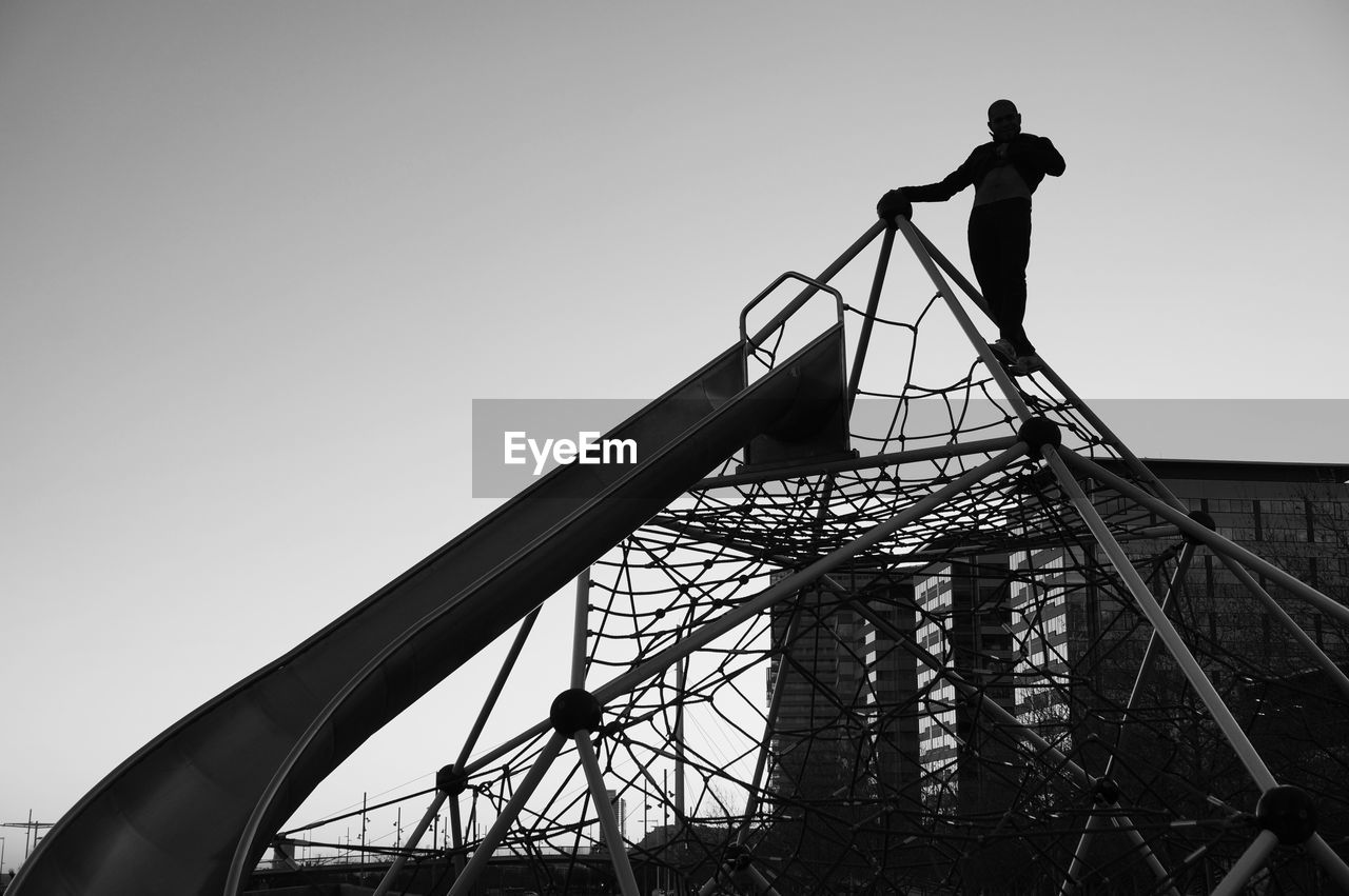 Low angle view of a man on jungle gym against clear sky
