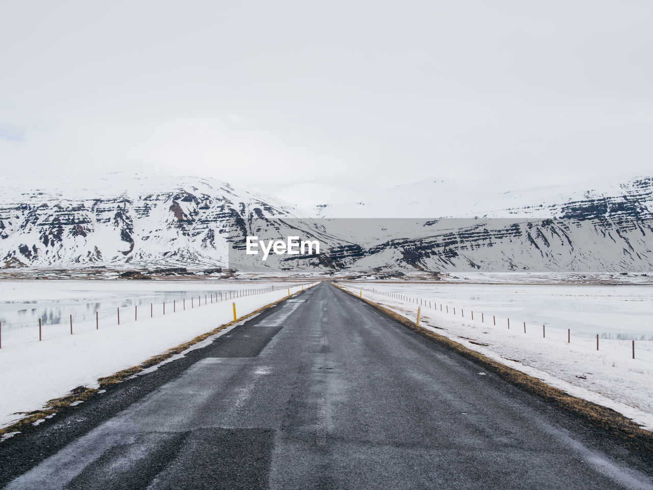 Empty road amidst landscape against sky during snowfall