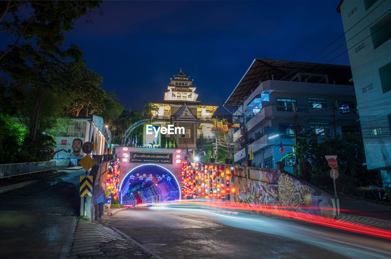 LIGHT TRAILS ON ROAD AMIDST BUILDINGS IN CITY AT NIGHT
