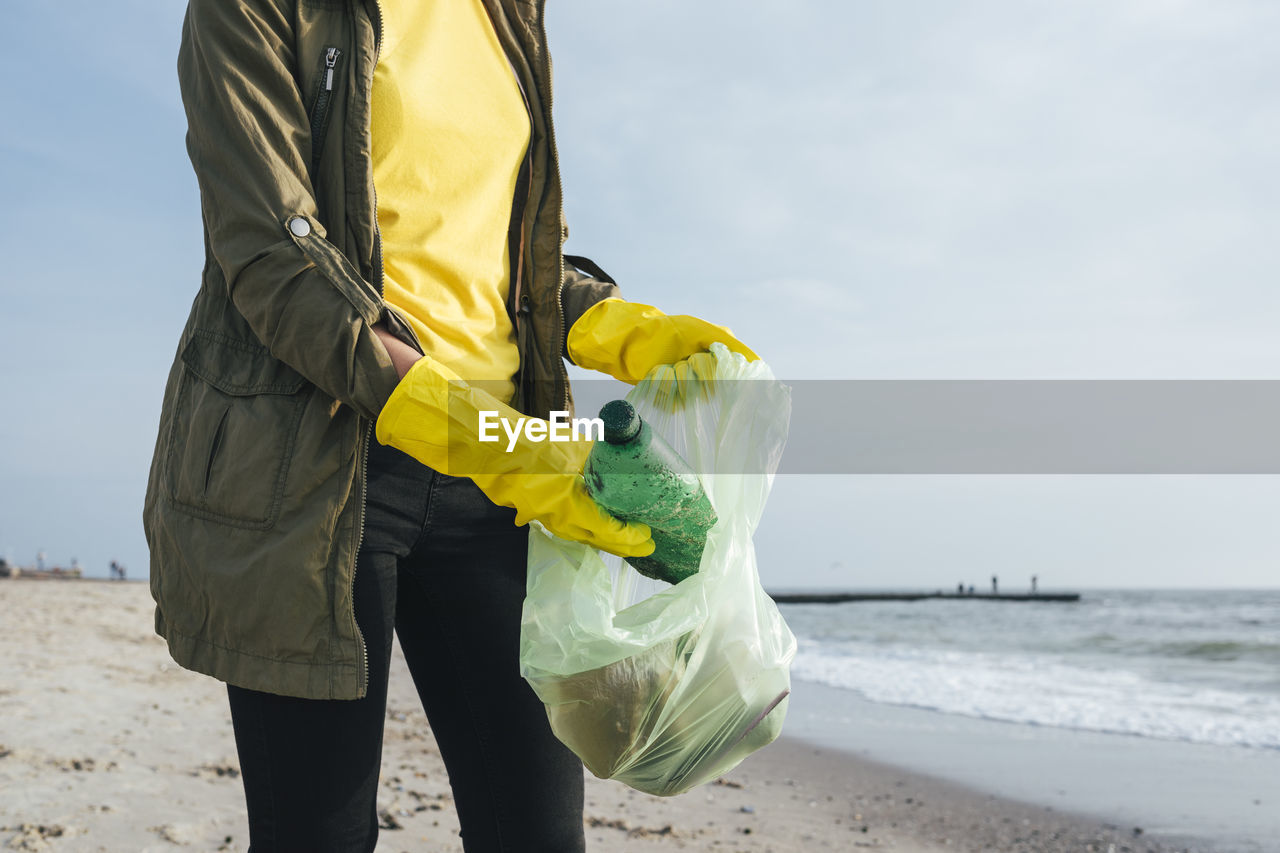 Woman wearing gloves collecting waste plastic bottles in garbage bag