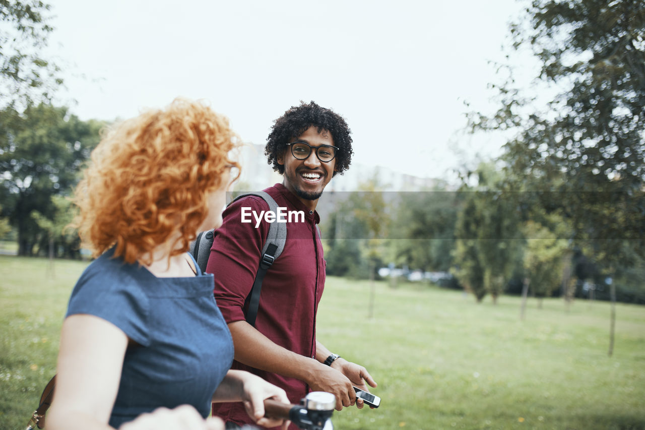 Friends walking in park, talking, woman pushing bicycle