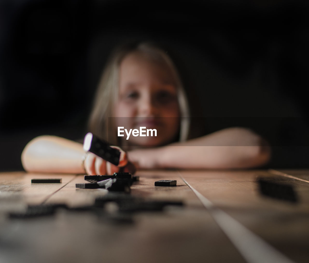 Portrait of girl playing dominoes at table against black background