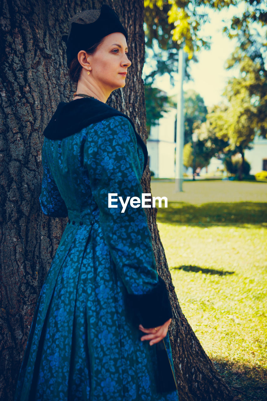 BEAUTIFUL WOMAN STANDING BY TREE TRUNK