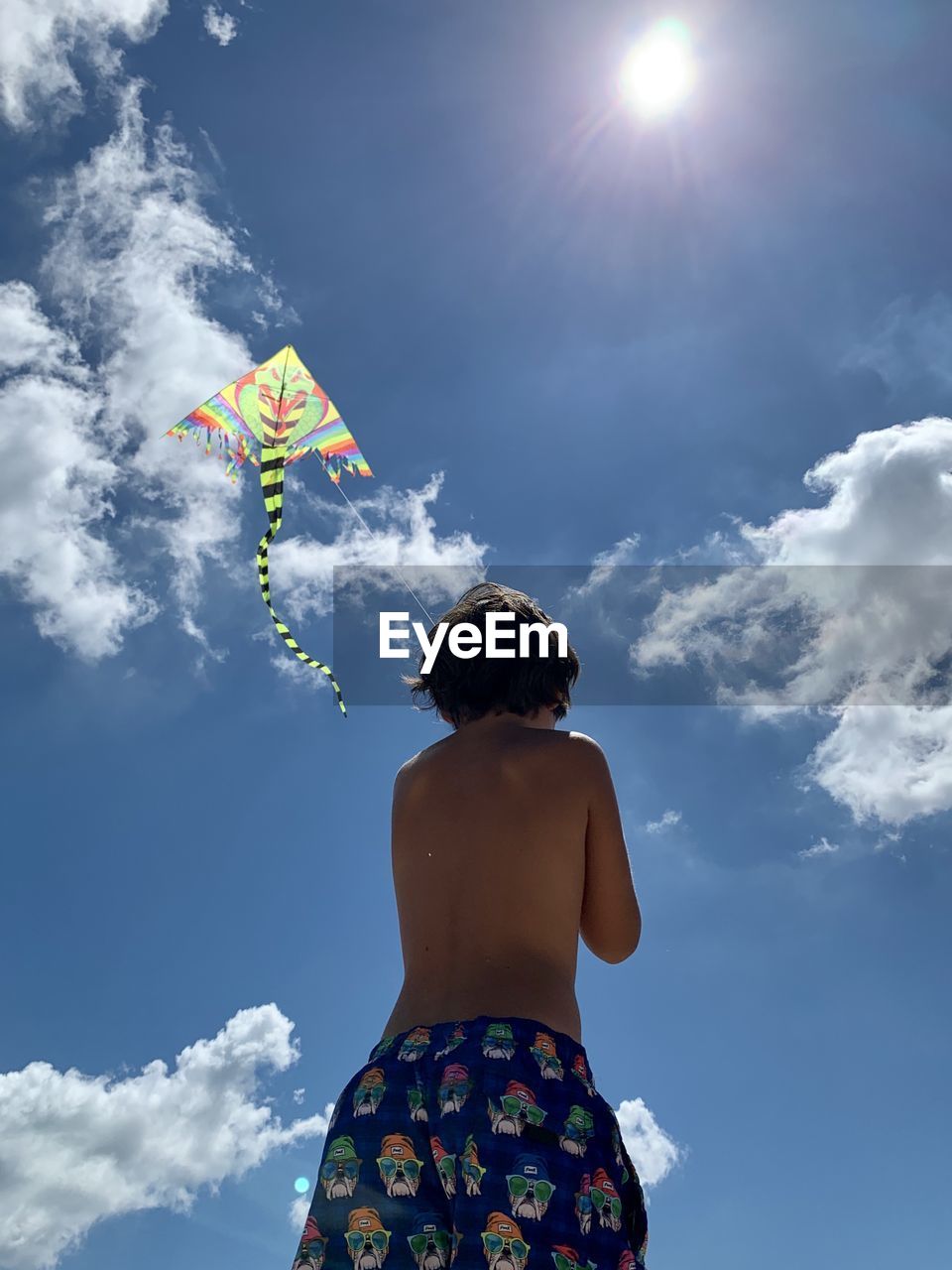 Rear view of boy flying kite standing against sky