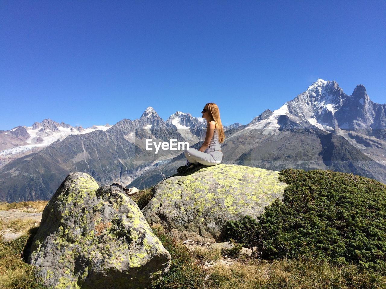 Side view of woman sitting on rock against mountains