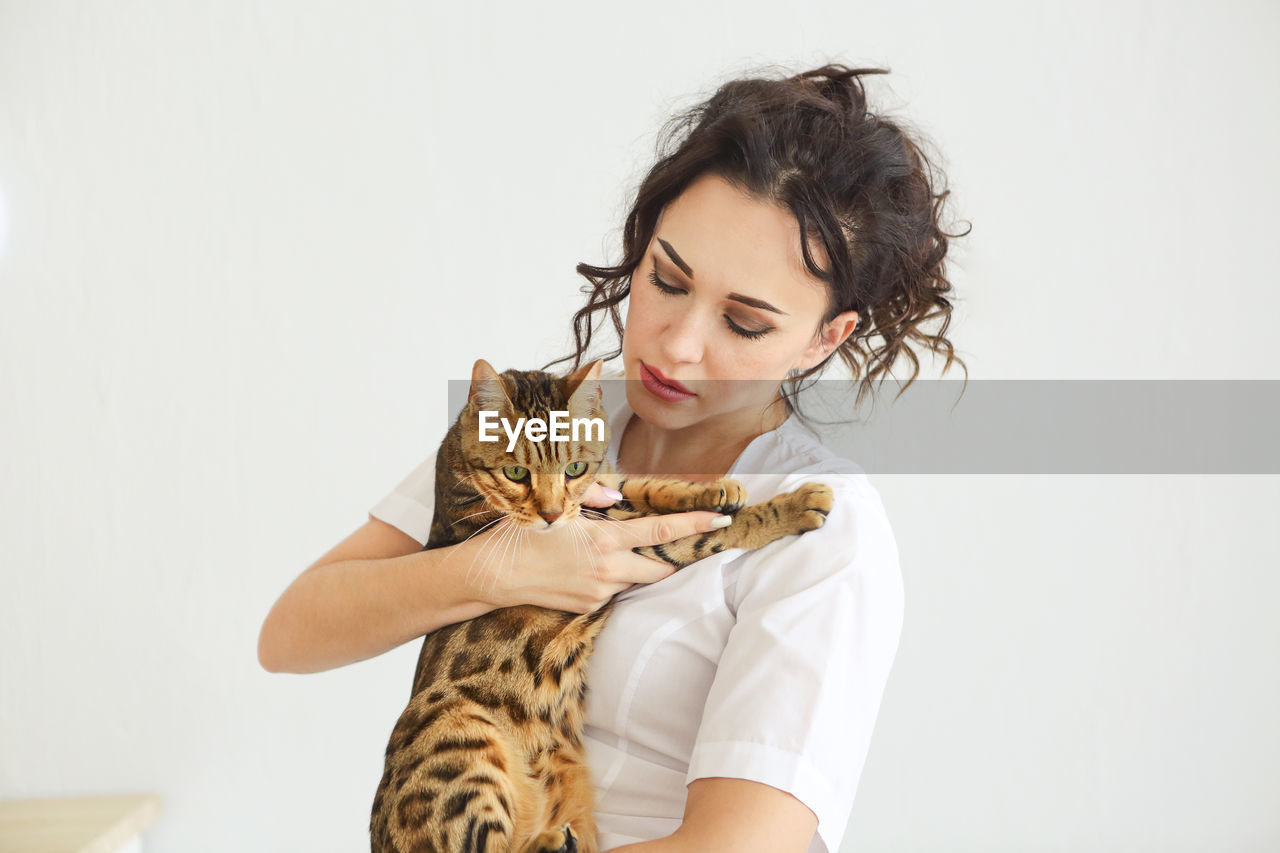 Portrait of a young woman with cat against white background