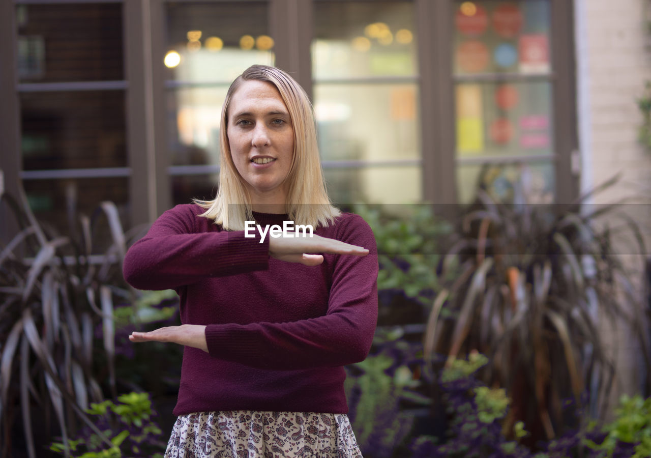 Portrait of woman gesturing while standing against plants