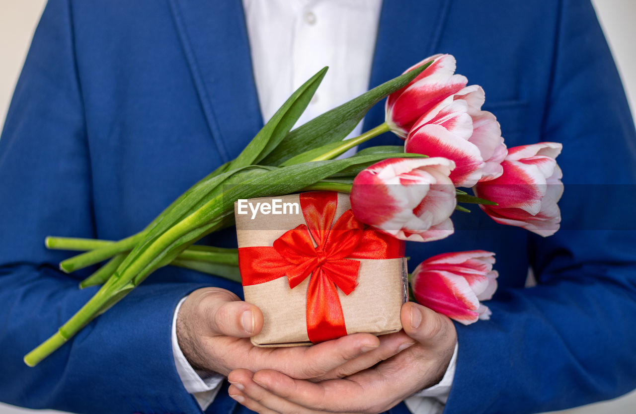Man holding one tulip flower in hand or in jacket on palm.male in office suit with gift box, bouquet