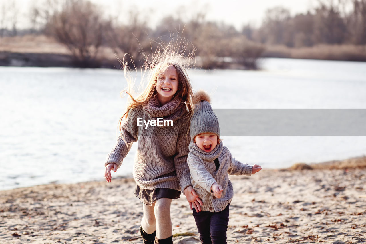 Portrait of happy girl with brother playing at lakeshore