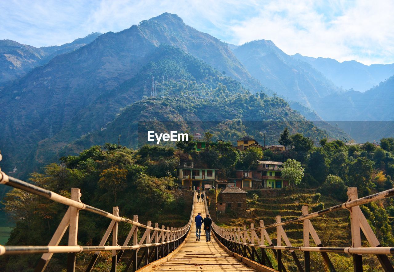 Rear view of men on footbridge against mountain
